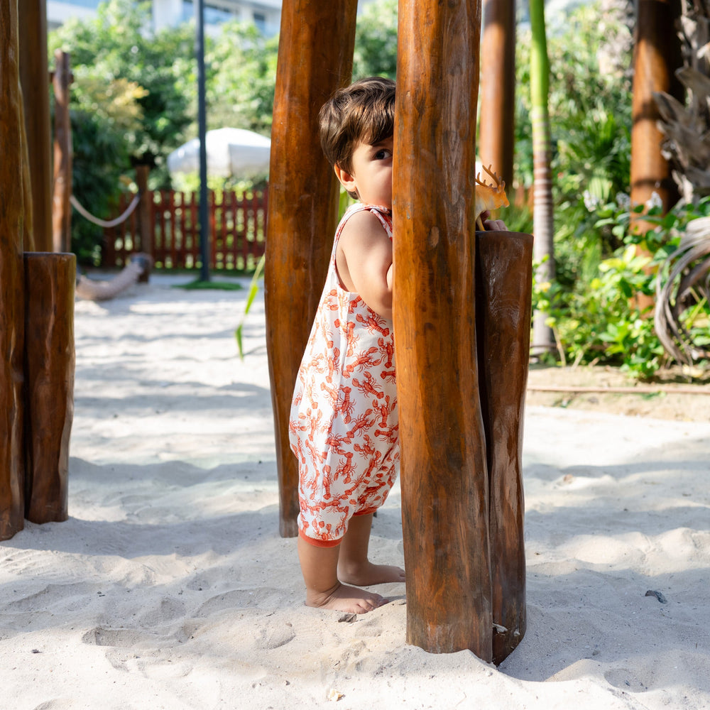 Child playing in a sandy area with wooden structures. Wearing cream handmade onesie with red lobster on it.