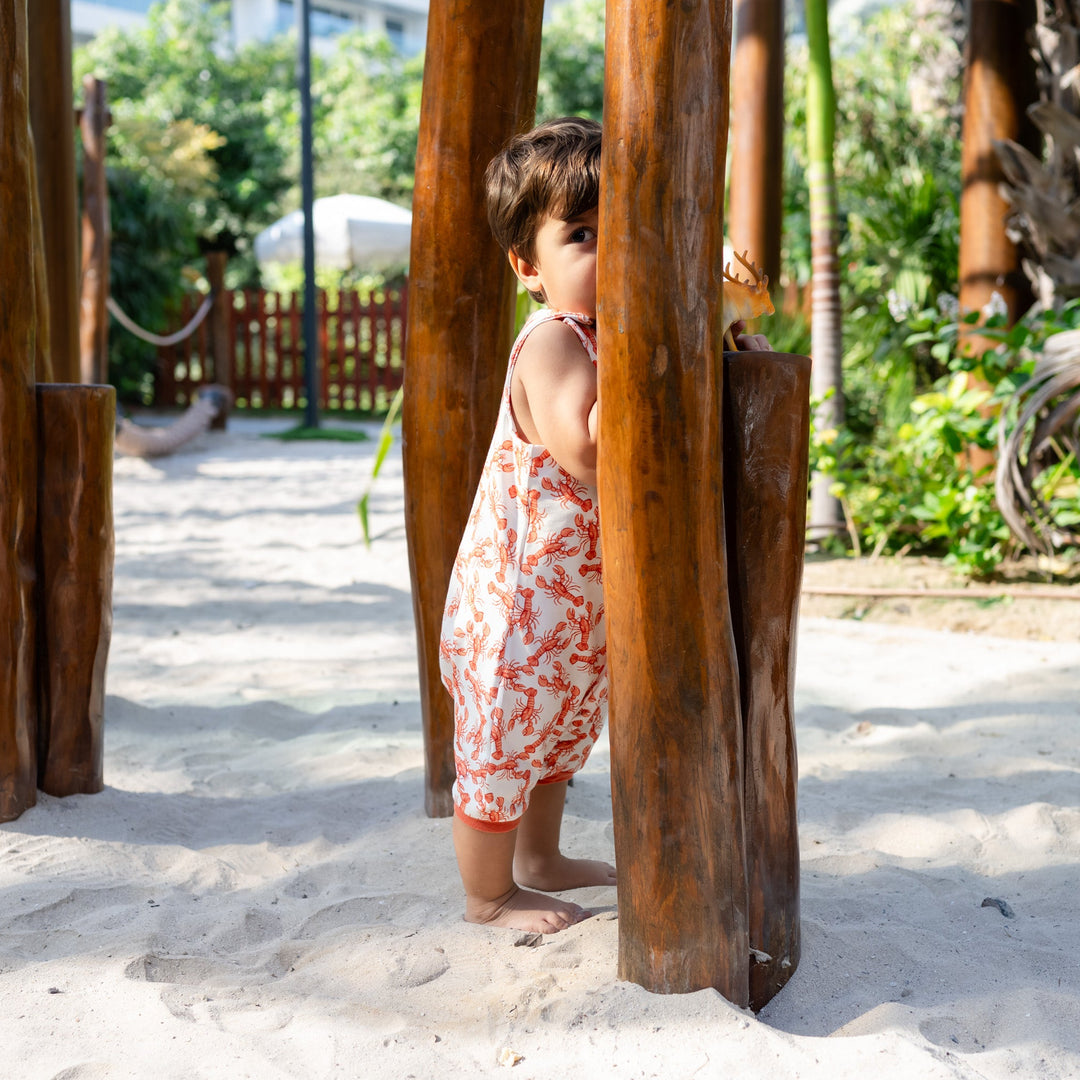 Child playing in a sandy area with wooden structures. Wearing cream handmade onesie with red lobster on it.