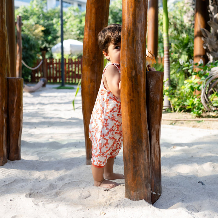Child playing in a sandy area with wooden structures. Wearing cream handmade onesie with red lobster on it.