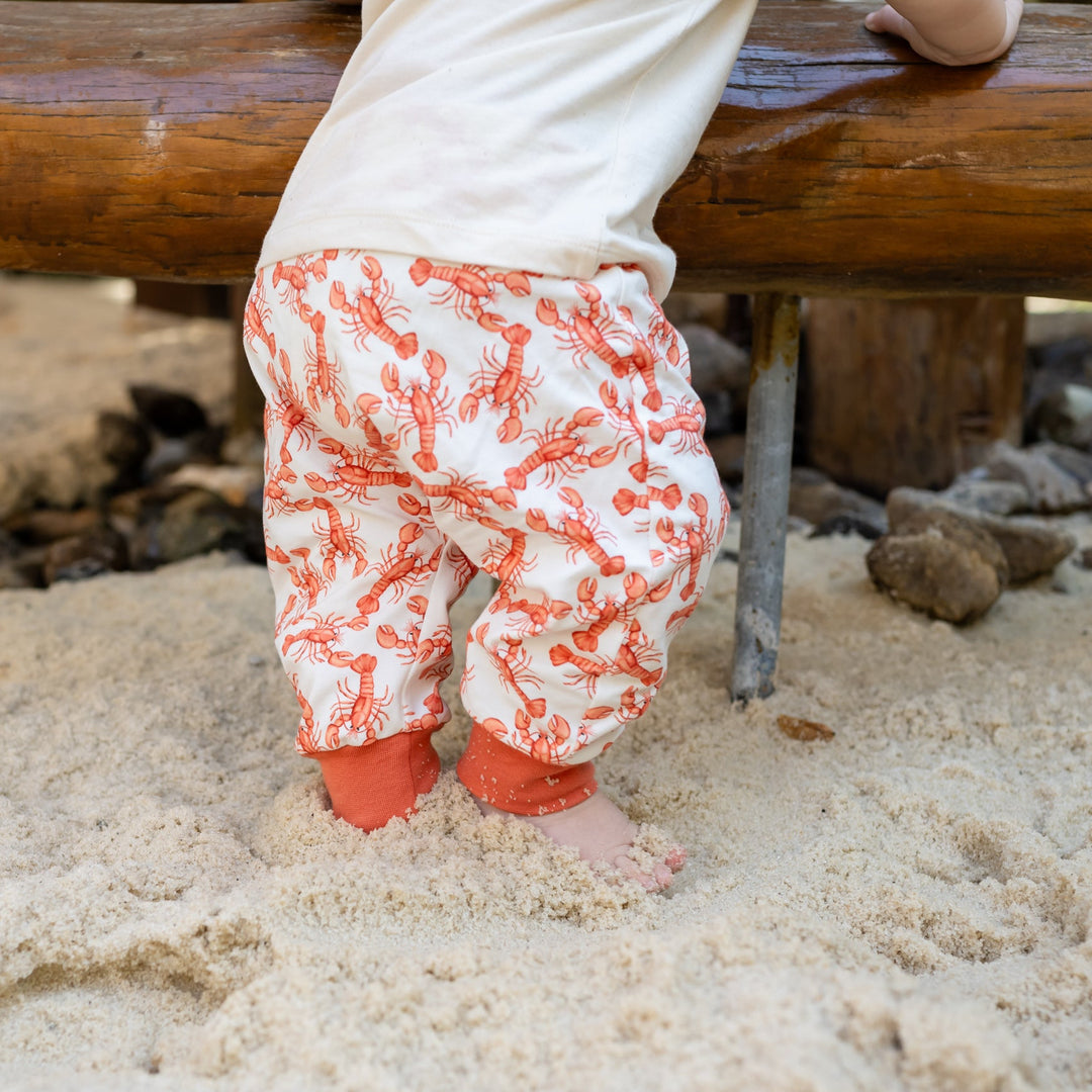 Baby standing in sand wearing a &
