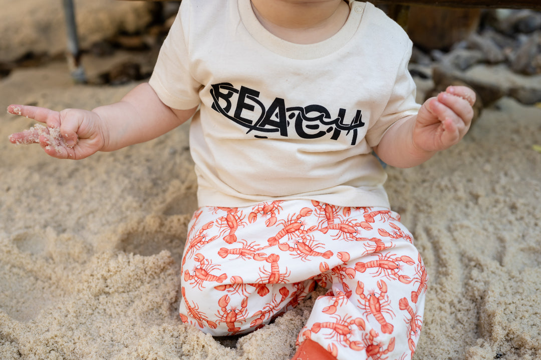 Baby sitting in sand wearing a &