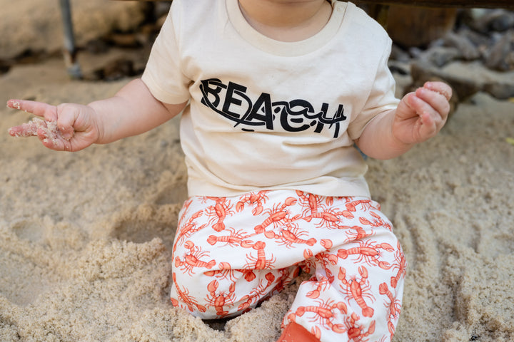 Baby sitting in sand wearing a &