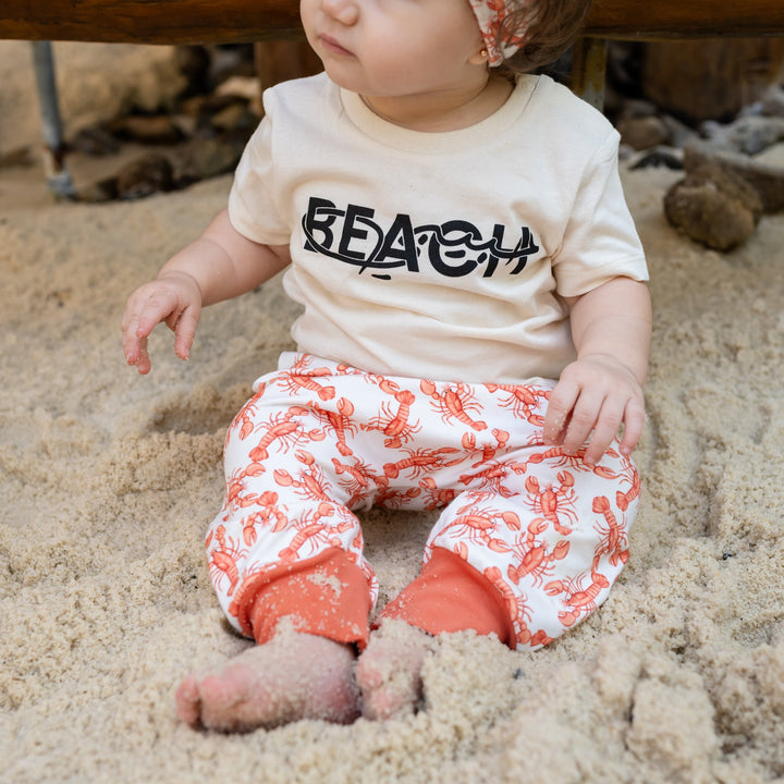 Baby sitting in sand wearing a &
