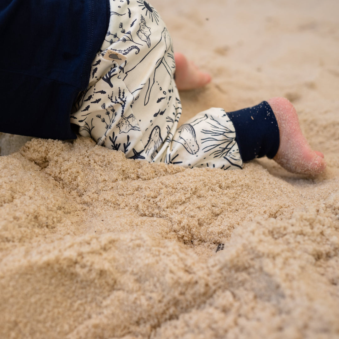 Child playing in sand with patterned pants and dark shoes