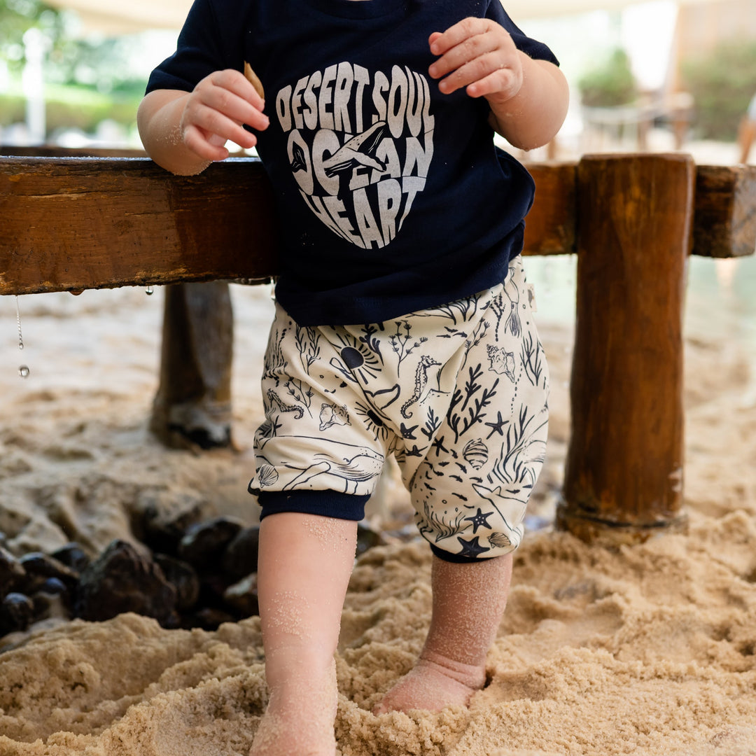 Child playing in a sandbox wearing a navy blue shirt with white text and patterned shorts.