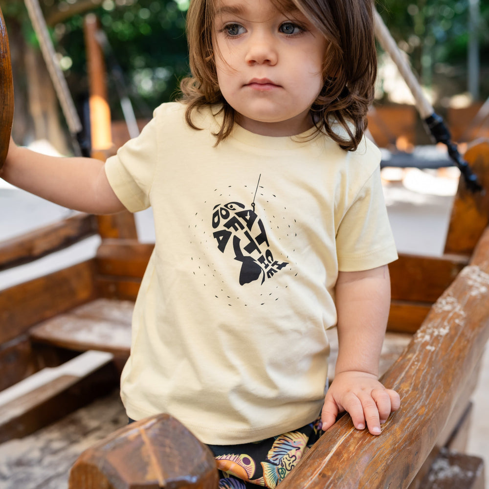 Child wearing a yellowt-shirt with a black fish design on a wooden playground.