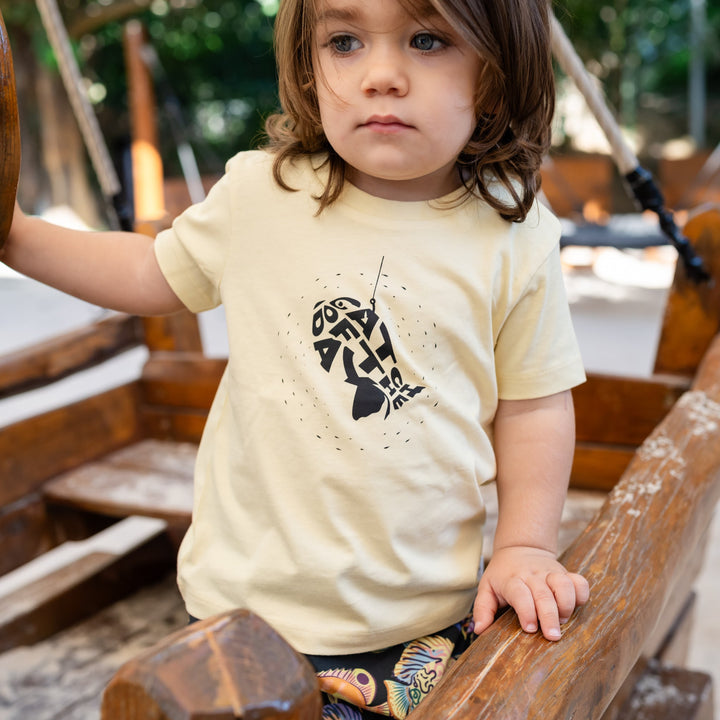 Child wearing a yellowt-shirt with a black fish design on a wooden playground.
