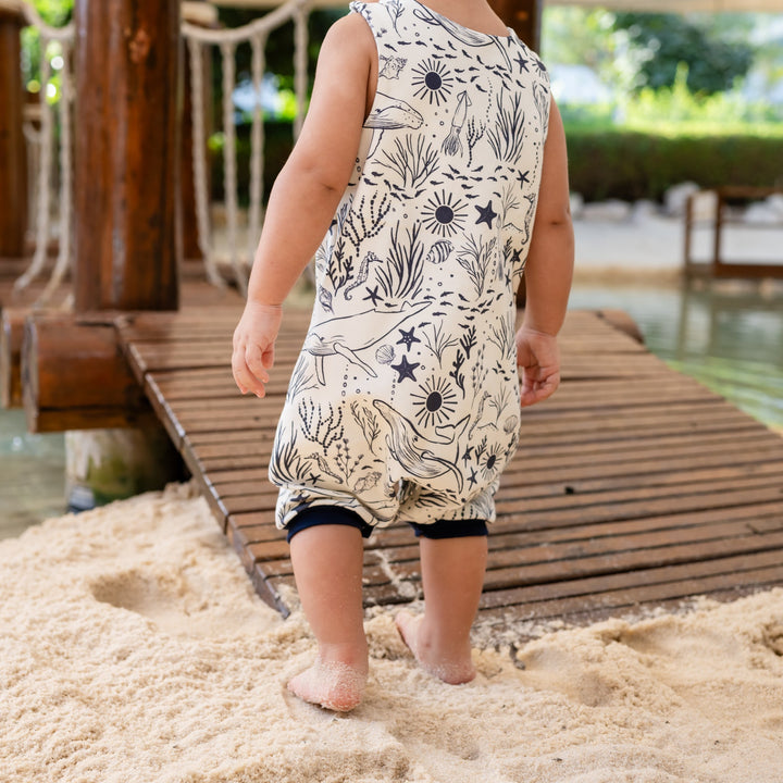 Child in a patterned dress standing on sand near a poolside.