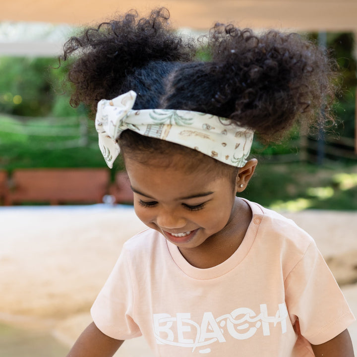 Child playing in a water puddle wearing a pink shirt with text and headband