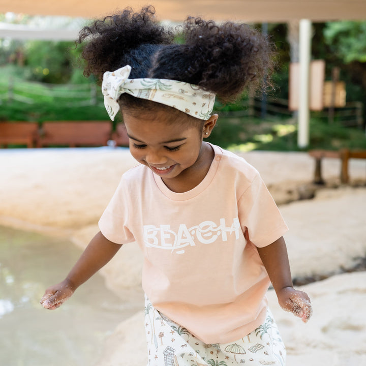Child playing in a water puddle wearing a pink shirt with text.