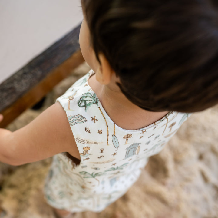 Child in a white dress with beach-themed print standing on a wooden step.