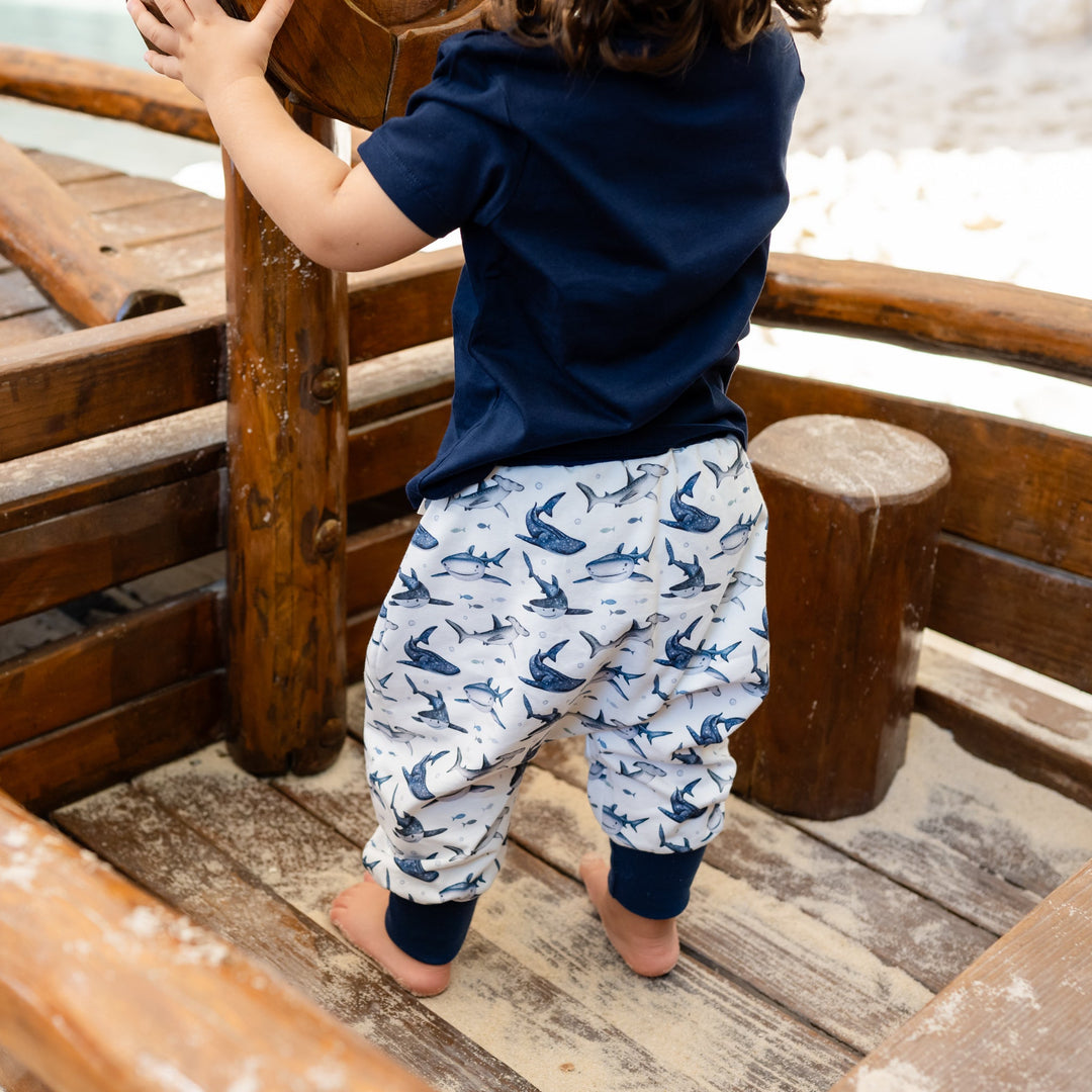 Child climbing a wooden structure in a sandy area wearing an organic pants and t-shirt sets with sharks on it