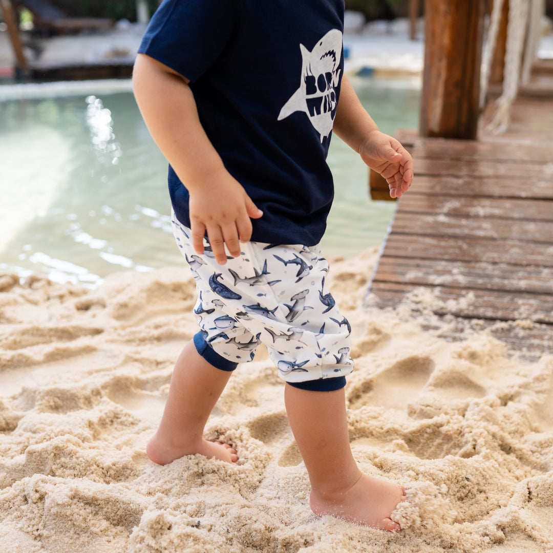 Child standing on a sandy beach wearing navy shorts with shark pattern