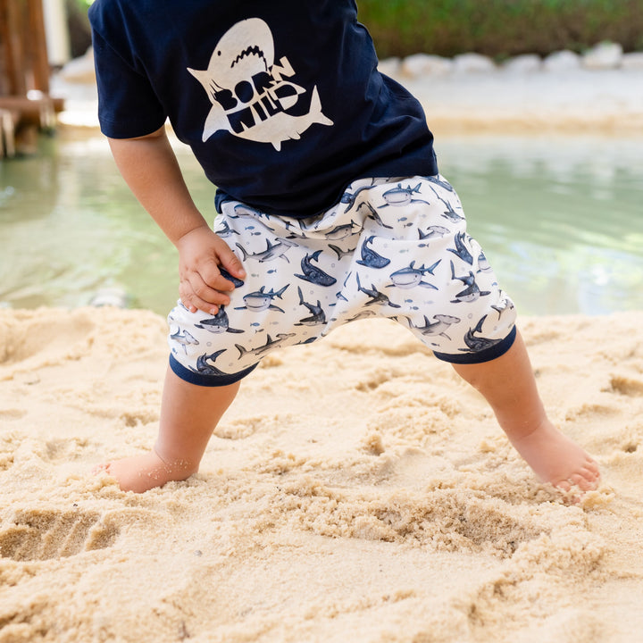 Child playing in sand wearing navy shirt with shark design and white shorts with shark pattern.